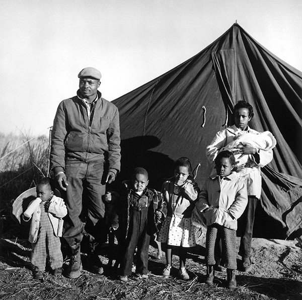 Family standing in front of a makeshift tent home.